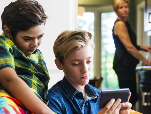 Two children looking at phone with concerned caregiver in background