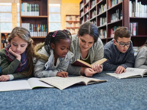 Students laying down reading in a school library with teacher