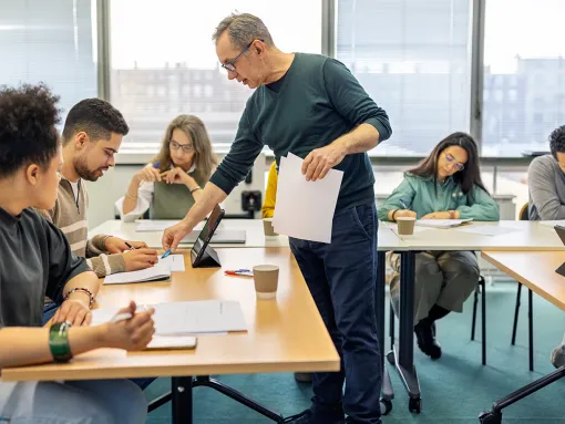 Senior professor teaching a student sitting at desk in adult education classroom